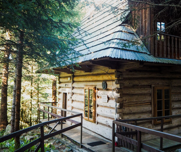 Domek pustelnika św. Brata Alberta na Kalatówkach: Drewniany domek pustelnika św. Brata Alberta, otoczony drzewami, z małym gankiem i stromym dachem. Współczesna fotografia ukazuje budynek wśród lasu.