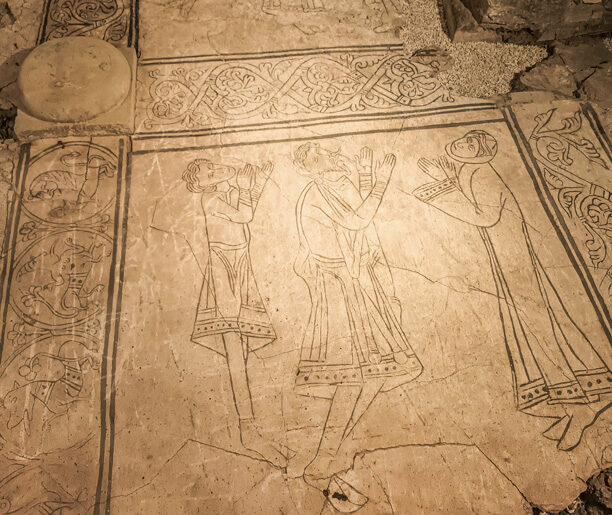 Fragment posadzki z wykutymi rysunkami postaci modlących się, otoczonych ornamentami roślinnymi. Ślady średniowiecznego kunsztu artystycznego.