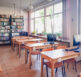 Sala komputerowa z rzędem drewnianych stołów wyposażonych w komputery, przy których znajdują się krzesła. Duże okna wpuszczają naturalne światło do wnętrza.